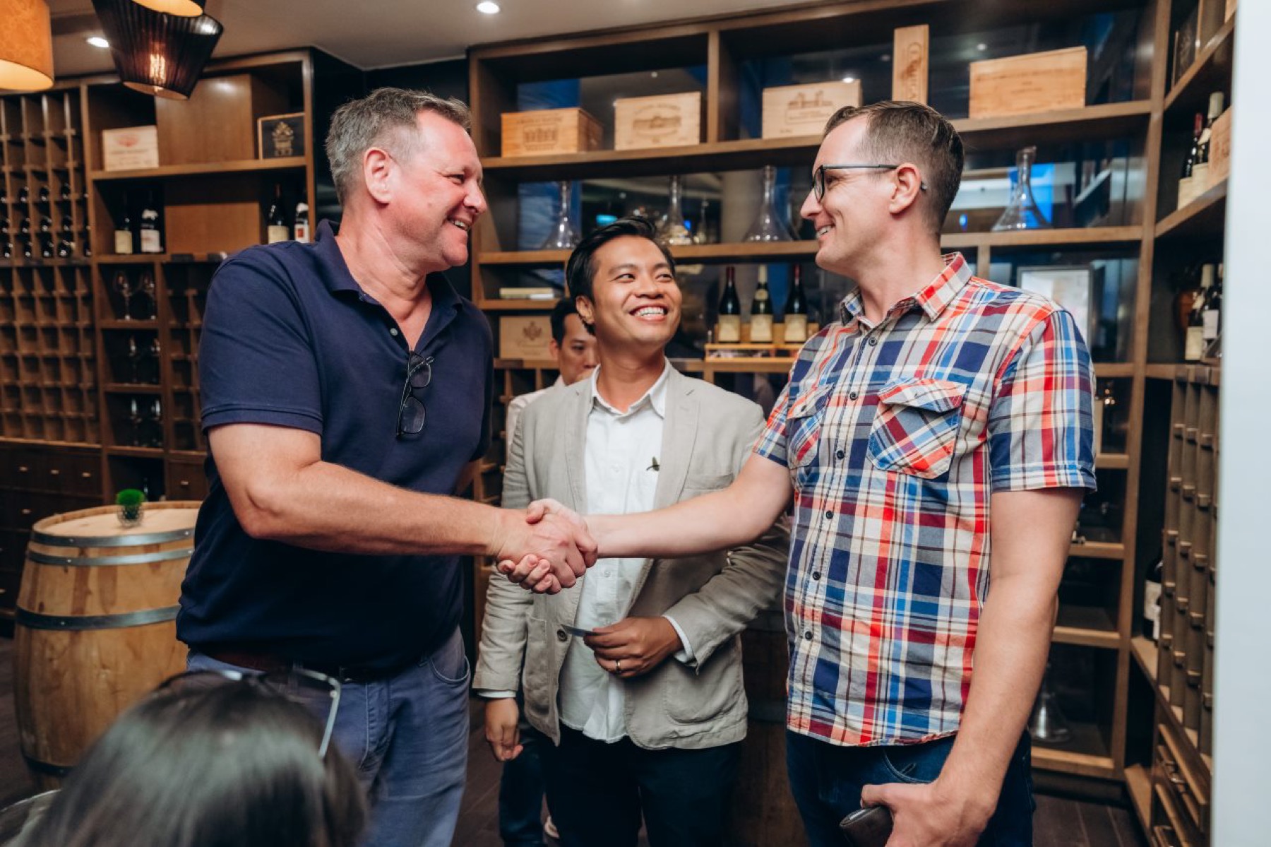 Three guests shaking hands in a wine room at an AusCham Sundowners